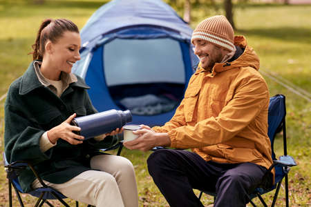 happy couple with thermos pouring tea at tent campの写真素材