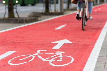 woman cycling along red bike lane road in cityの写真素材