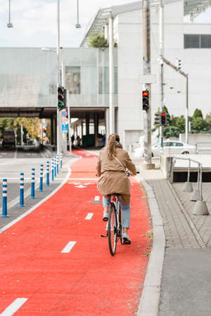 woman cycling along red bike lane road in cityの写真素材