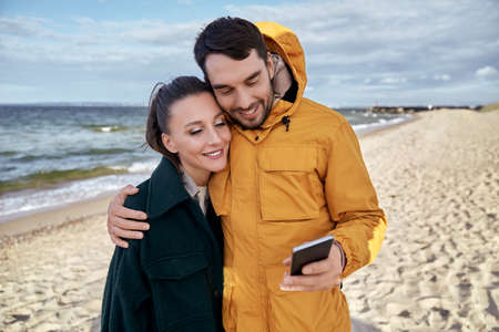 couple with smartphone on autumn beachの写真素材