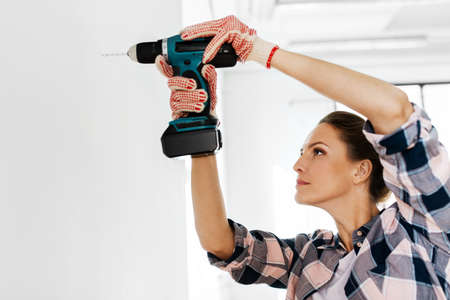 woman with perforator drilling wall at home