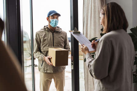delivery man in mask with box and customer at homeの写真素材