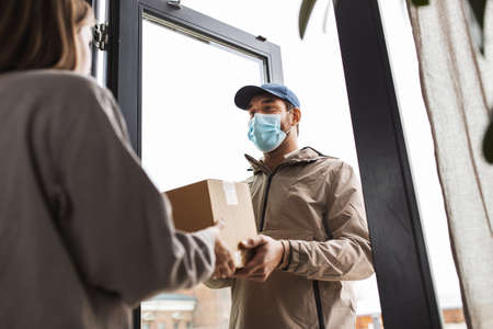 delivery man in mask giving parcel to customerの写真素材