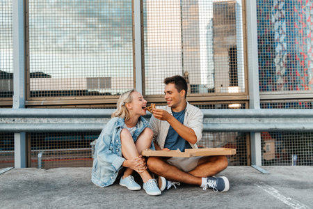 happy couple eating pizza on city roof top parkingの写真素材