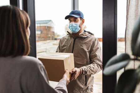 delivery man in mask giving parcel to customerの写真素材