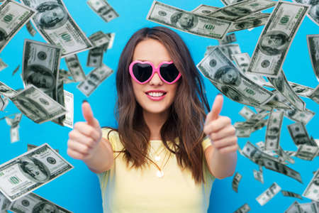 woman in sunglasses shows thumbs up over moneyの写真素材