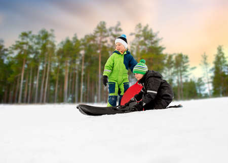 kids sliding on sleds down snow hill in winterの写真素材