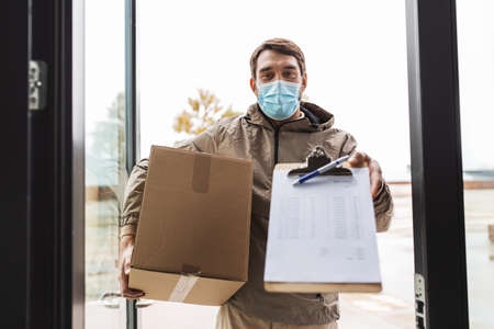 delivery man in mask with parcel box and clipboardの写真素材
