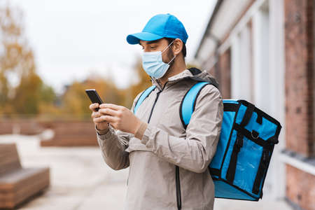 delivery man in mask with phone and thermal bagの写真素材