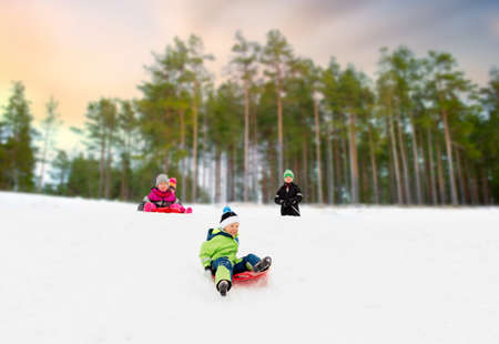 kids sliding on sleds down snow hill in winterの写真素材
