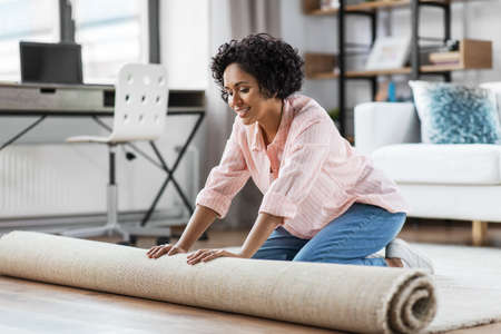 young woman unfolding carpet at homeの写真素材