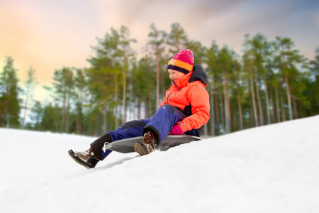 happy girl sliding down on sled in winterの写真素材