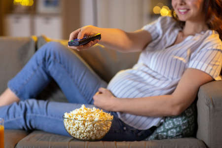 pregnant woman with remote control watching tvの写真素材