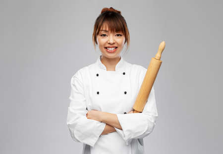 smiling female chef or baker with rolling pinの写真素材
