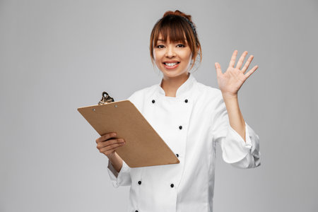 smiling female chef with clipboard waving handの写真素材
