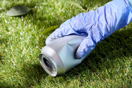 close up of hand in glove with used can on grass