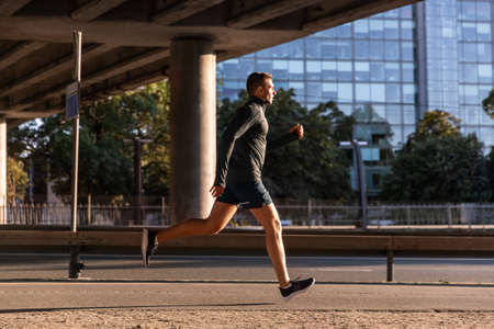 young man running outdoors under bridgeの写真素材
