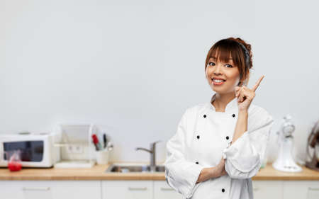smiling female chef pointing finger up on kitchen