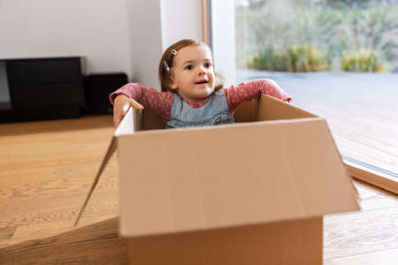 little baby girl sitting in cardboard box at homeの写真素材