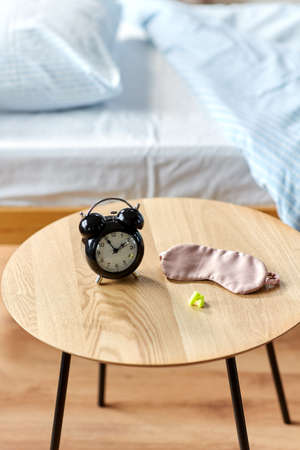 alarm clock, earplugs and sleeping mask on table
