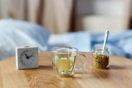 alarm clock and cup of chamomile tea on tableの写真素材