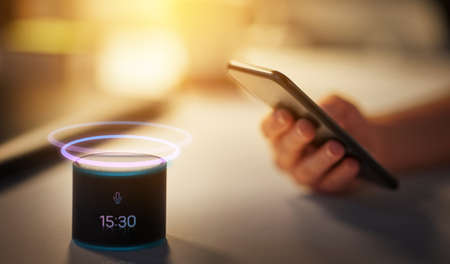 hand with smartphone and time on smart speakerの写真素材