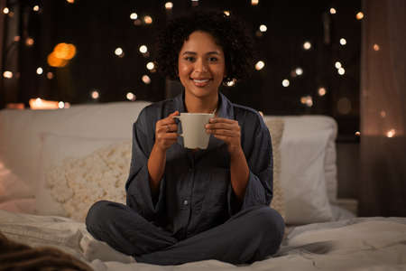 happy woman with coffee sitting in bed at nightの写真素材