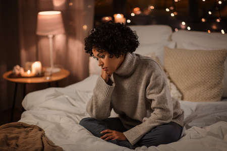 sad woman in sweater on bed at home at night