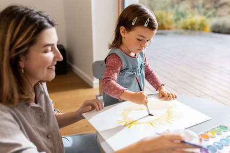 mother with little daughter drawing sun at homeの写真素材