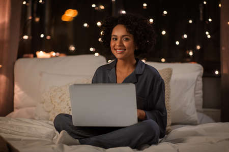 happy woman with laptop sitting in bed at night