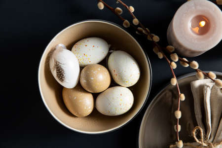 easter eggs, willow and candle on black table