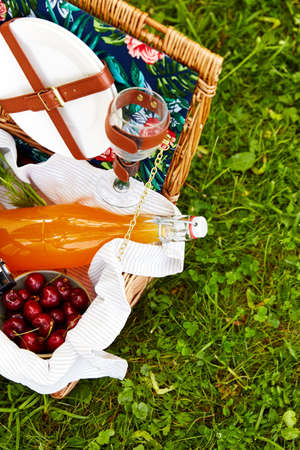 leisure, food and summer concept - close up of juice, cherry, book and camera in picnic basketの写真素材
