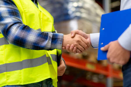 worker and businessman shaking hands at warehouseの写真素材