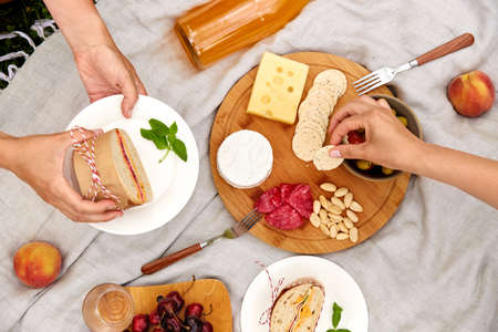 close up of hands with food and drinks on picnic