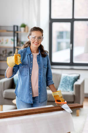 woman with saw sawing wooden board at homeの写真素材