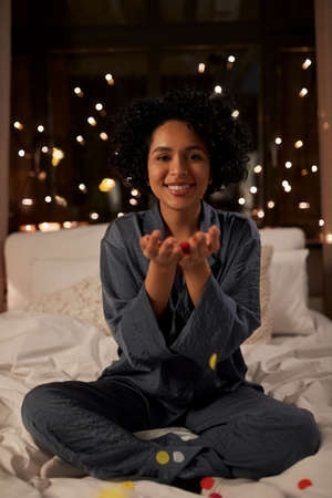 woman blowing confetti in bed at night at home