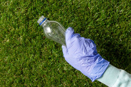 hand in glove picking plastic bottle from grassの写真素材