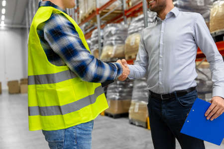 worker and businessman shaking hands at warehouseの写真素材