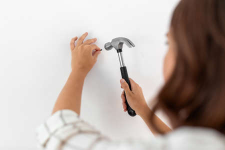 close up of woman hammering nail to wall at homeの写真素材