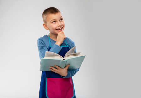 little boy in apron reading cook book and thinking