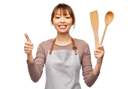 happy woman in apron with wooden spoon and spatulaの写真素材