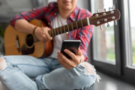 man with guitar and phone sitting on sillの写真素材