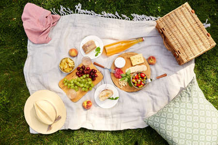 food, drinks and picnic basket on blanket on grassの写真素材