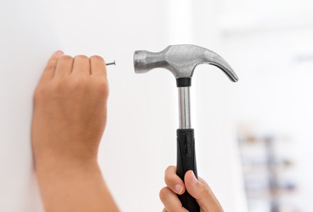close up of hands hammering nail to wall at homeの写真素材