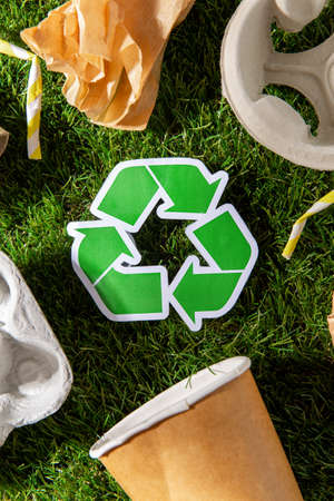 green recycling sign and paper waste on grass