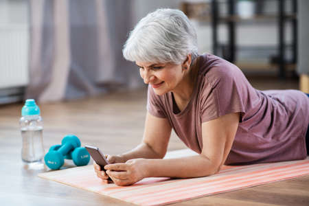 senior woman with smartphone exercising at homeの写真素材