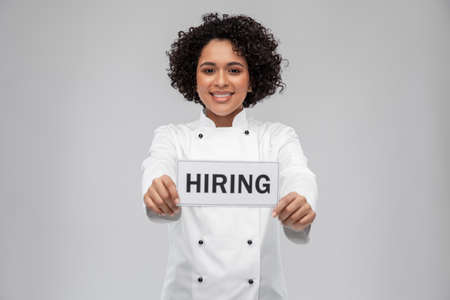 smiling female chef in jacket holding hiring sign