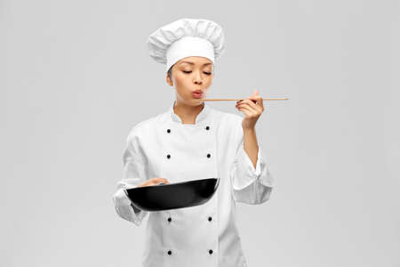 female chef with frying pan tasting foodの写真素材