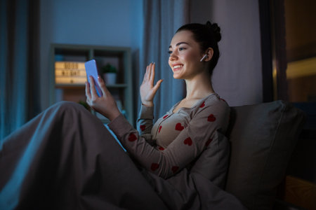 teenage girl with phone pc has video call in bedの写真素材