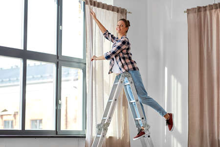 woman on ladder hanging curtains at homeの写真素材